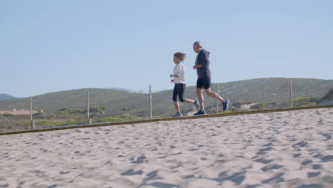 Cheerful-senior-couple-running-along-path-on-sandy-beach