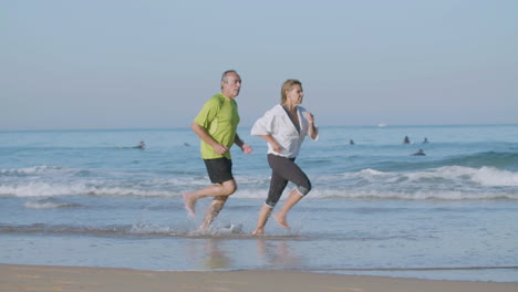 Woman-running-ahead-her-husband-while-they-jogging-on-beach