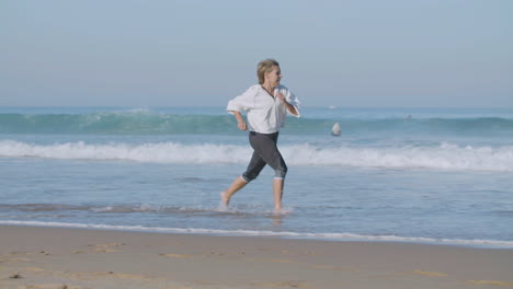 Happy-Caucasian-woman-running-barefoot-along-ocean-coast