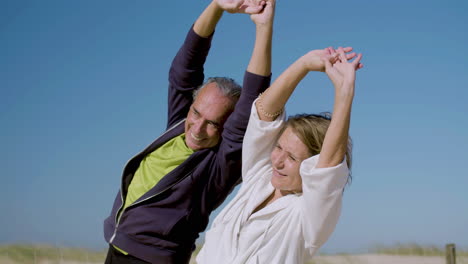 Happy-senior-couple-raising-arms-up-and-bending-to-sides-outdoor