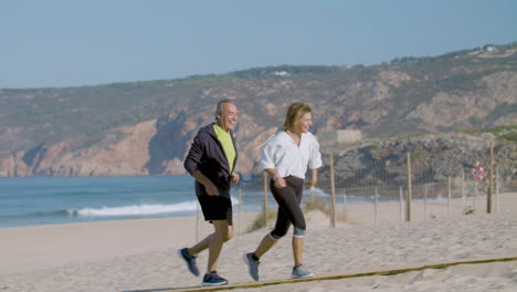 Smiling-mature-man-and-woman-running-on-beach-on-summer-day