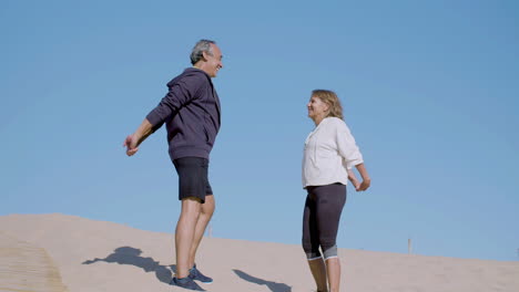 Senior-couple-standing-on-sandy-seashore-and-stretching-arms