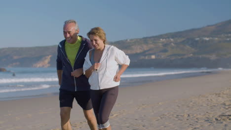 Cheerful-man-and-woman-jogging-along-ocean-coast-on-summer-day