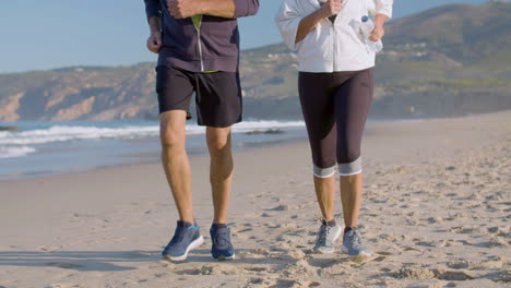 Elderly-couple-in-sportswear-running-on-sandy-beach-together