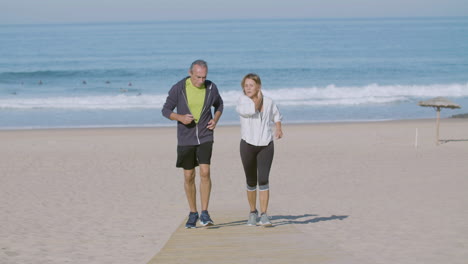Cheerful-mature-couple-running-uphill-on-sandy-beach