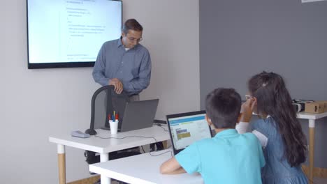Computer-science-teacher-standing-at-his-desk-in-class