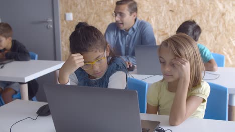 Computer-science-teacher-sitting-at-desk-near-schoolboy