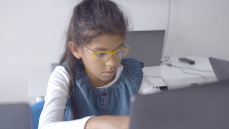 Serious-smart-schoolgirl-in-glasses-sitting-at-desk