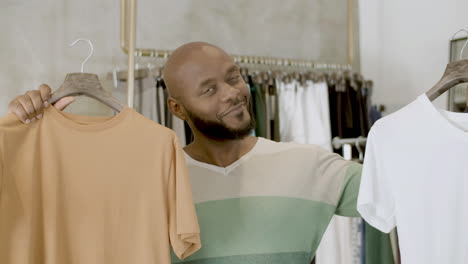 Bearded-black-guy-choosing-between-two-T-shirts-in-clothing-shop