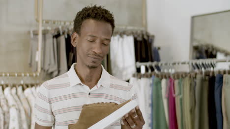 Thin-African-American-guy-examining-shoe-before-purchase.
