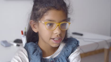 Fröhliches,-Intelligentes-Lateinamerikanisches-Schulmädchen-Mit-Brille,-Das-Am-Schreibtisch-Sitzt