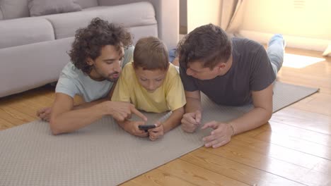 Focused-kid-lying-on-floor-near-dads-and-using-app