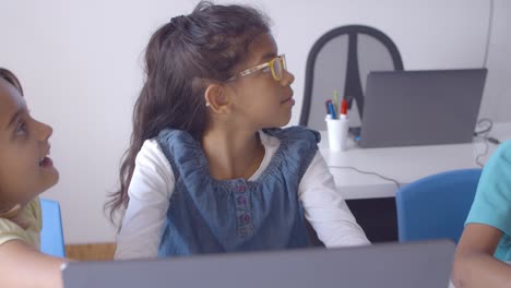 Focused-schoolgirl-in-glasses-using-laptop-in-class