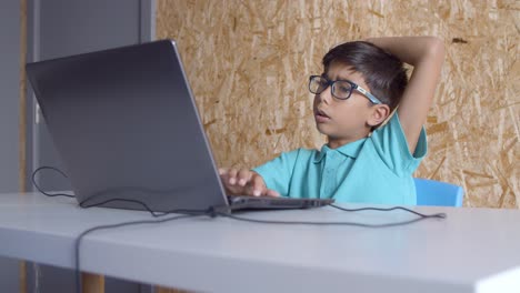 Focused-schoolboy-in-glasses-sitting-at-desks-with-laptop