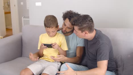 Focused-boy-sitting-on-dads-lap-and-playing-online-game