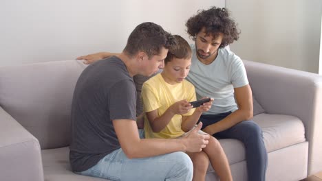 Two-dads-helping-son-with-online-app-on-mobile-phone