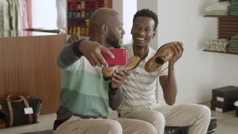 Happy-black-male-couple-taking-selfie-holding-leather-shoes.