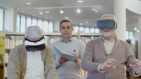 Senior-men-using-virtual-reality-glasses-with-teacher-in-library