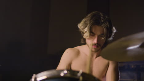 Young-shirtless-male-drummer-with-beard-playing-drums