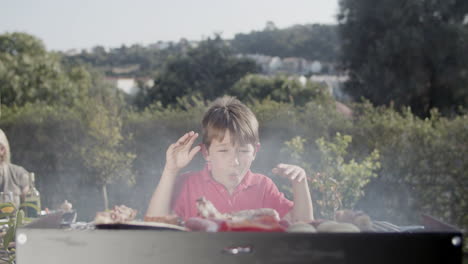 Funny-preteen-boy-waving-hands-and-blowing-at-barbecue-grill