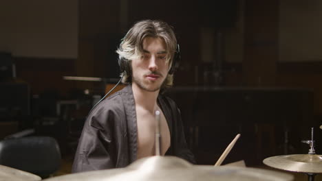 Young-male-drummer-in-undone-black-robe-playing-drums