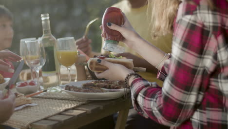 Close-up-of-teenage-girl-squeezing-ketchup-on-her-hotdog