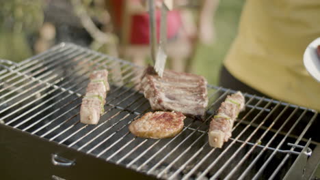 Close-up-of-man-putting-sausage-from-barbecue-grill-to-plate