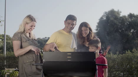 Happy-family-standing-together-at-barbecue-grill-watching-meat