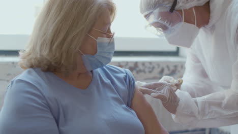 Medium-shot-of-nurse-vaccinating-senior-woman-against-covid