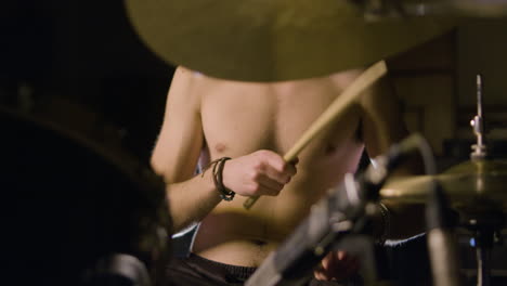 Young-shirtless-male-drummer-playing-drums-at-music-studio