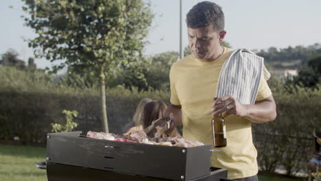 Smiling-man-turning-over-meat-on-barbecue-grill-outdoors