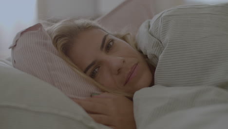 Cheerful-Caucasian-woman-lying-in-bed-under-blanket-and-smiling