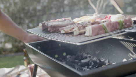 Barbecue-Grill-Mit-Fleisch-Und-Mann,-Der-Kohle-Umrührt-Und-Ausbläst