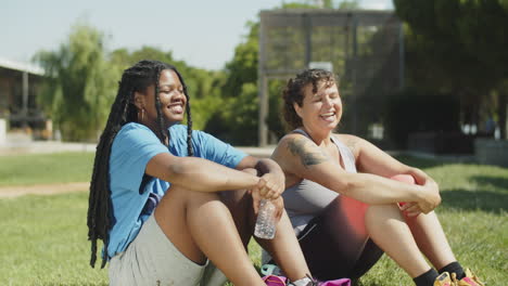 Side-view-of-smiling-friends-resting-on-lawn-after-workout