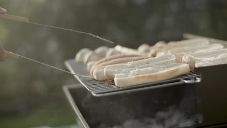 Man-turning-over-bread-for-hotdogs-on-barbecue-grill