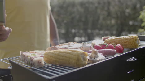Man-with-tweezers-watching-grilling-meat-and-vegetables