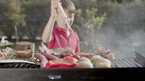 Happy-preteen-boy-taking-meat-with-fork-from-grill-to-eat-it