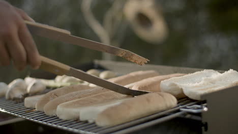 Male-hand-putting-bread-for-hotdog-on-barbecue-grill