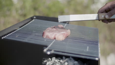 Nahaufnahme-Eines-Barbecue-Grills-Und-Einer-Metallpinzette,-Die-Ein-Steak-Hineinlegt