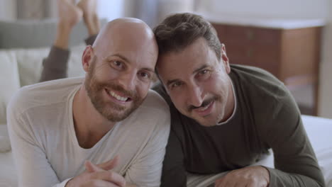 Fröhliche-Homosexuelle-Männer-Liegen-Auf-Dem-Bett-Und-Lächeln-In-Die-Kamera