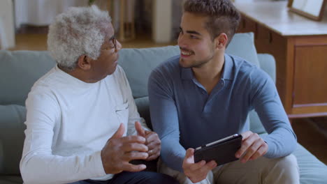 Bearded-Caucasian-guy-helping-senior-Black-man-with-using-tablet