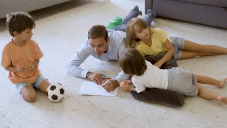 Sibling-kids-and-dad-lying-on-warm-floor-with-cushions