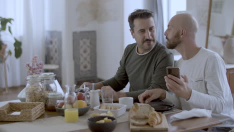 Homosexual-couple-looking-at-phone-screen-while-having-breakfast