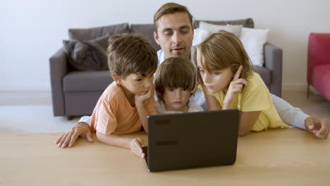 Cheerful-dad-reading-tale-to-pensive-kids-from-laptop