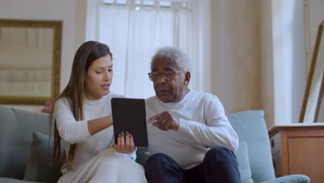 Young-woman-helping-her-grandpa-with-using-tablet.