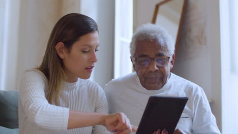 Young-Caucasian-girl-helping-her-grandpa-with-using-tablet.