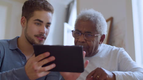 Young-Caucasian-guy-helping-his-grandpa-with-using-tablet.