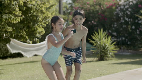 Two-children-jumping-in-swimming-pool,-holding-action-camera.