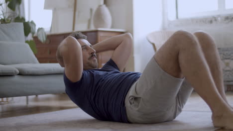 Handsome-bearded-man-doing-sit-ups-on-floor-at-home