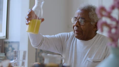 Closeup-of-Black-senior-man-pouring-orange-juice-in-glass.